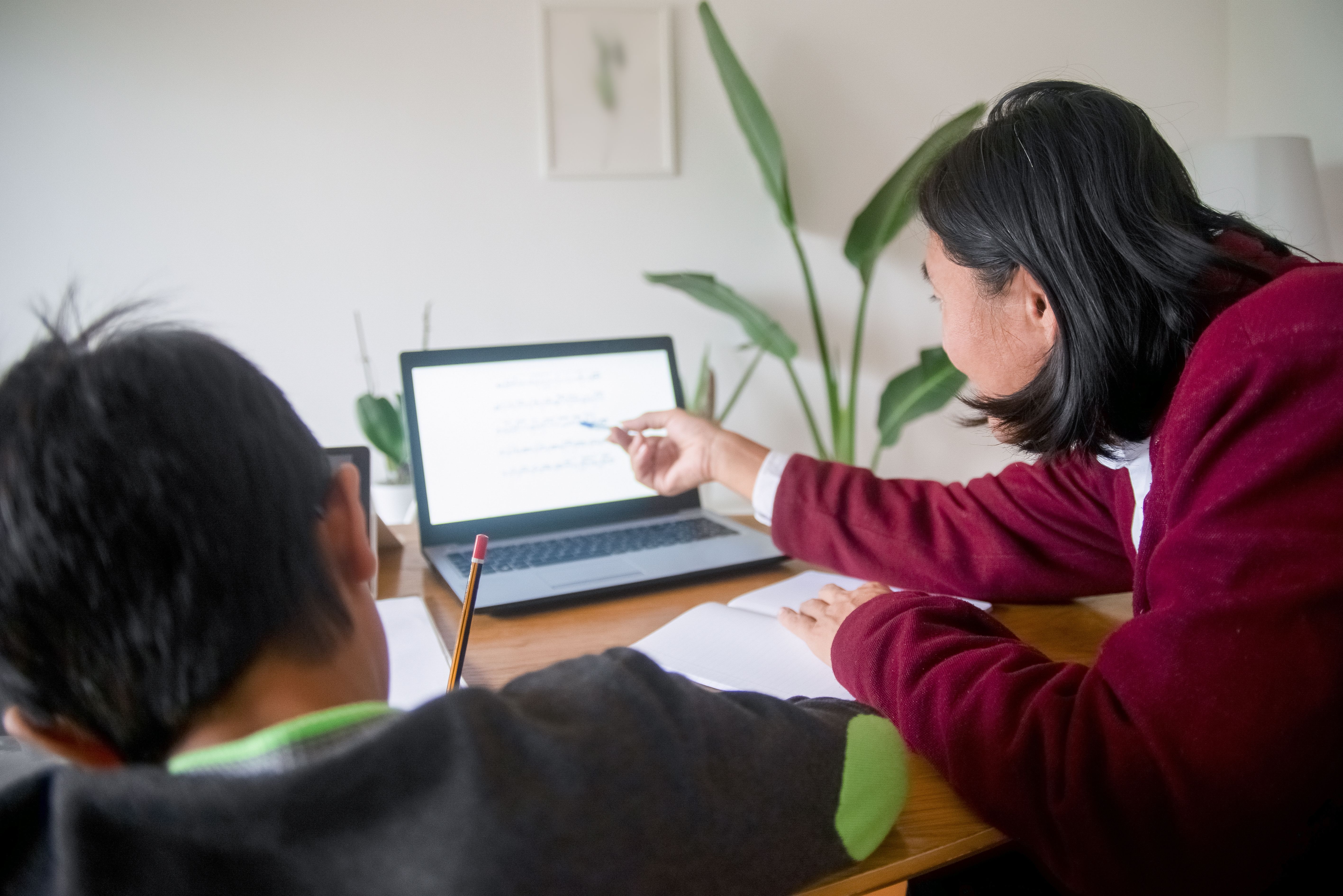 A parent helping a child learn at home using a laptop and notebook