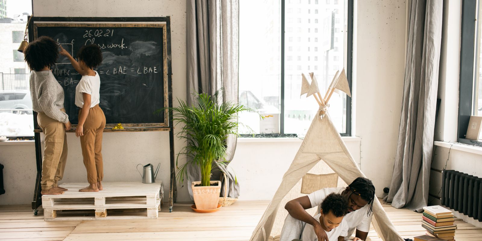 Two parents sitting on the floor helping their children with homework and writing on a blackboard
